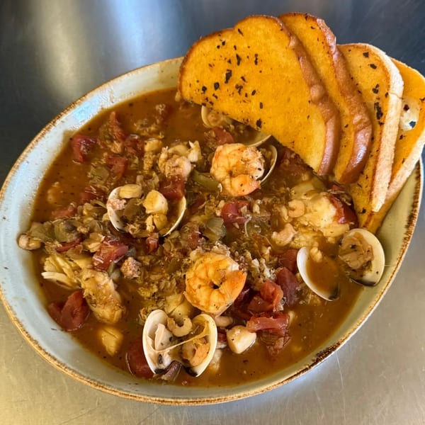 A bowl of seafood cioppino with shrimp, clams, and tomatoes, served with garlic bread.