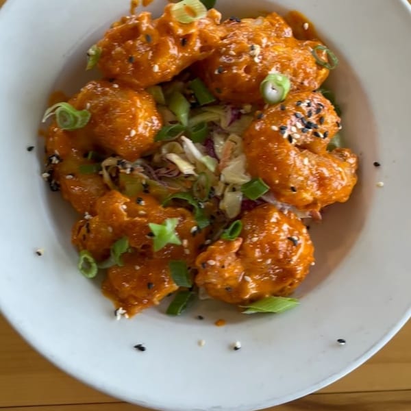 A white bowl filled with orange-glazed shrimp, topped with sesame seeds and green onions.