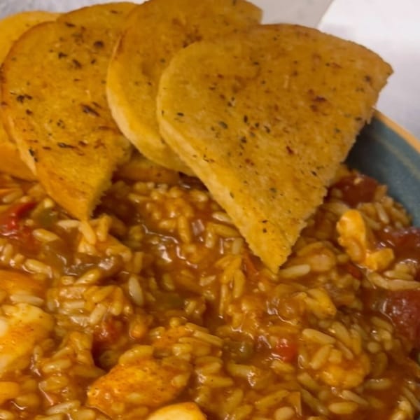 Close-up of The Sardine Can's seafood jambalaya with garlic bread slices.