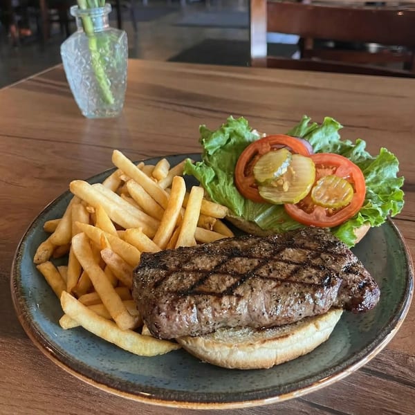 Grilled steak sandwich with lettuce, tomato, pickles, and a side of french fries on a blue plate.
