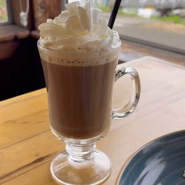 A glass mug of coffee with whipped cream and a straw on a wooden table.