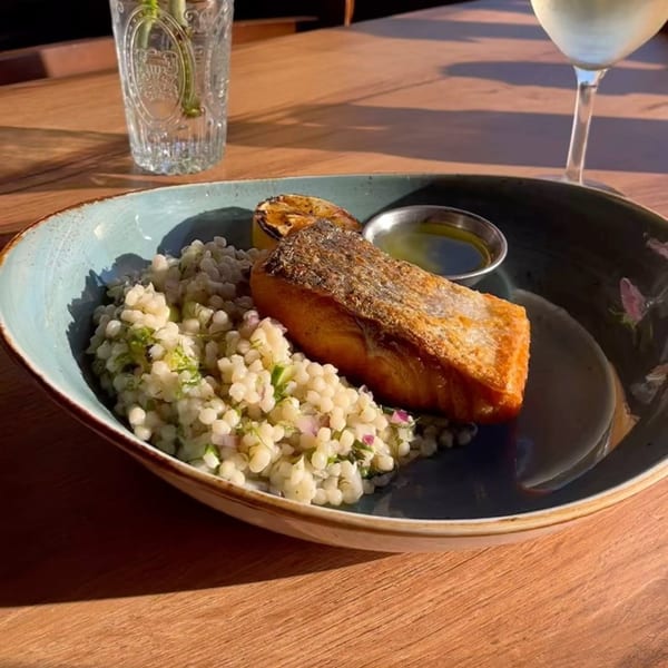 Seared salmon with couscous, grilled lemon, and a side of sauce on a blue plate.